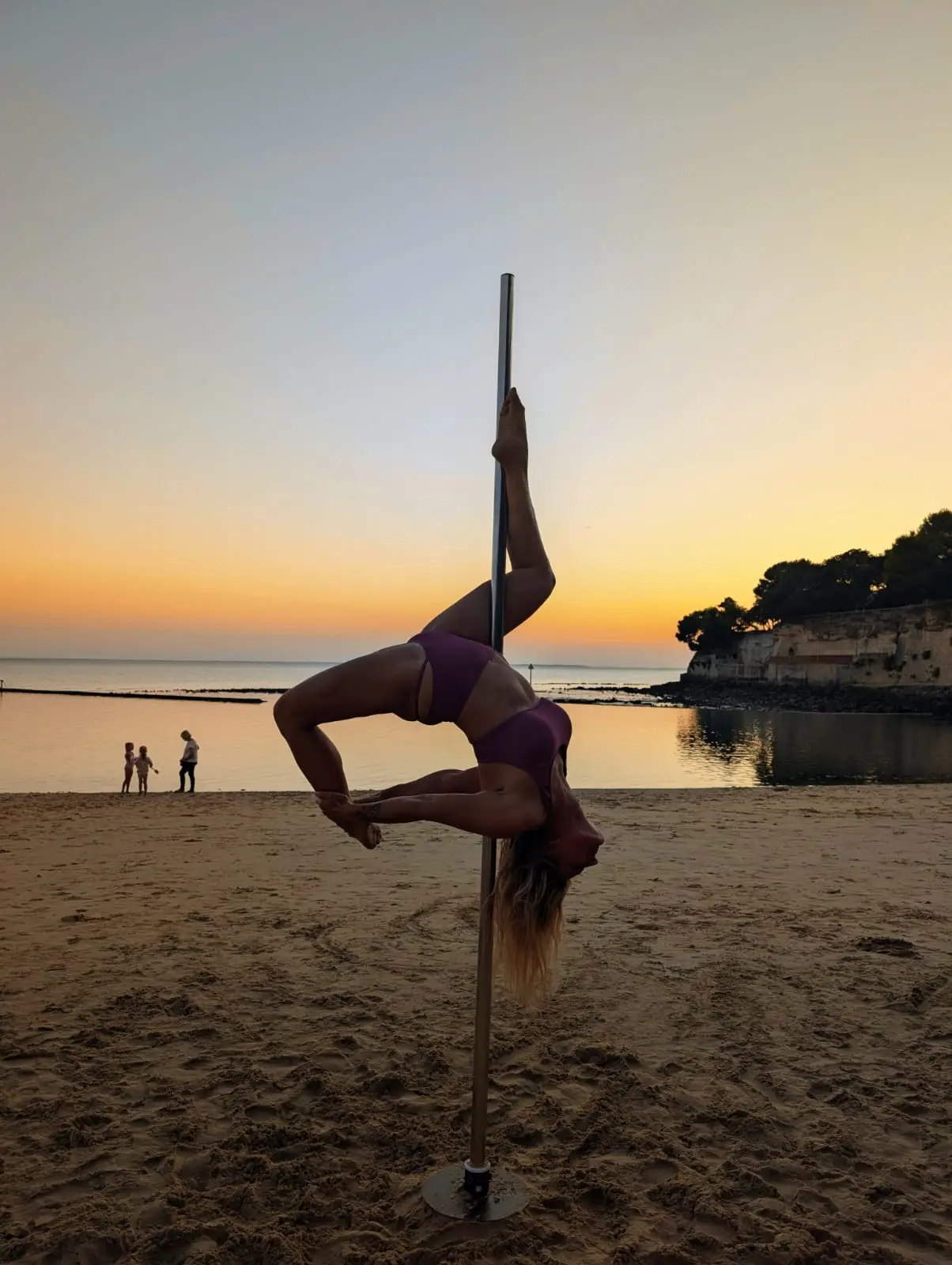 Danseuse en équilibre inversé sur le pôle, dos cambré, devant la mer au soleil couchant