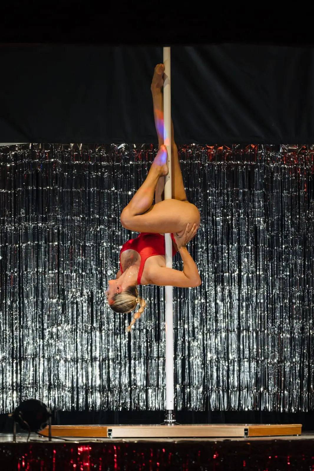 Danseuse en tenue rouge, en figure inversée le long du pôle, sur la scène d’un spectacle