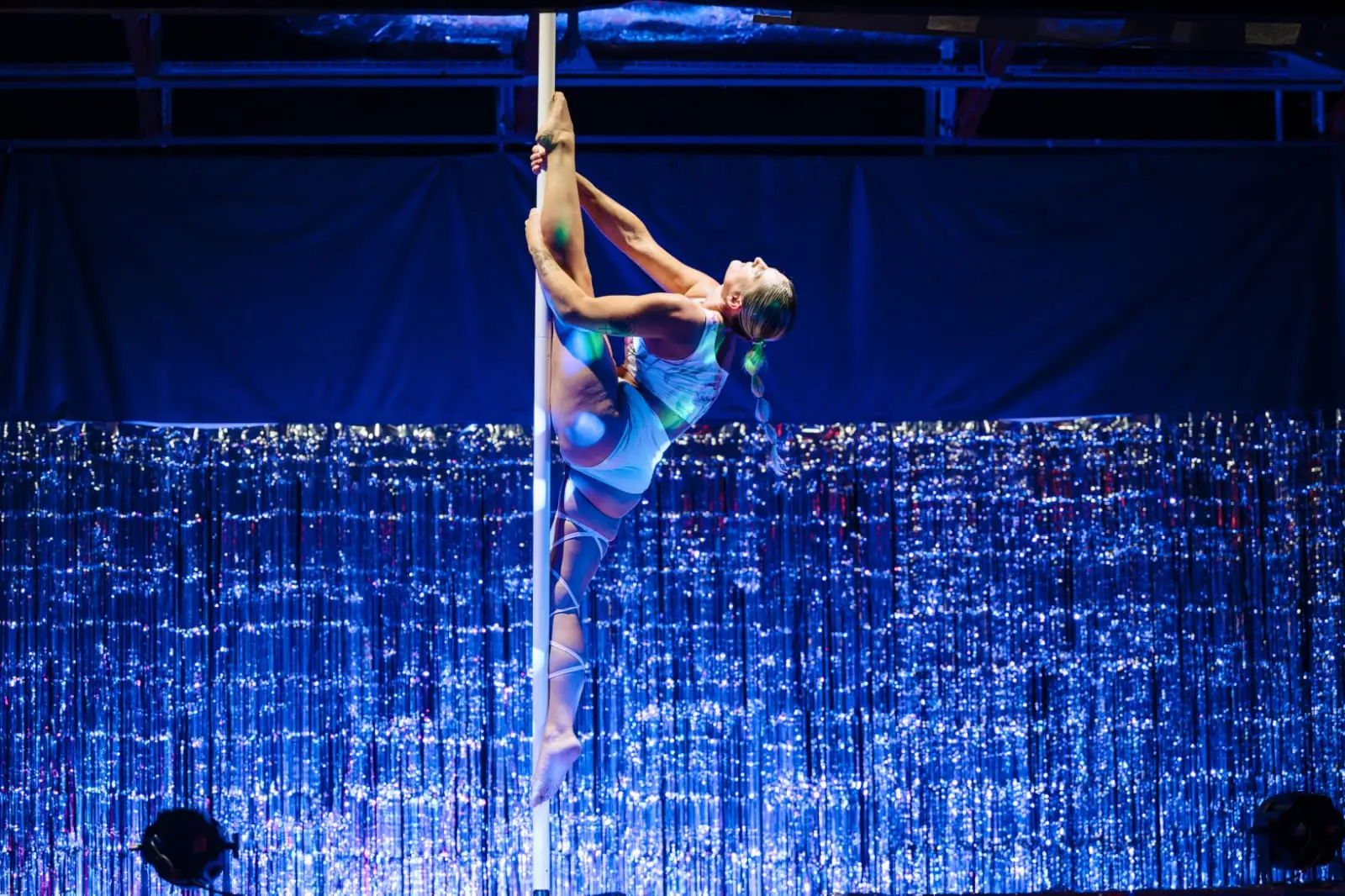 Danseuse cambrée contre le pôle, une jambe fléchie, sous une lumière bleue de scène